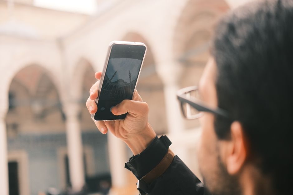 A person using a smartphone with a mosque in the background, representing the Nusuk app